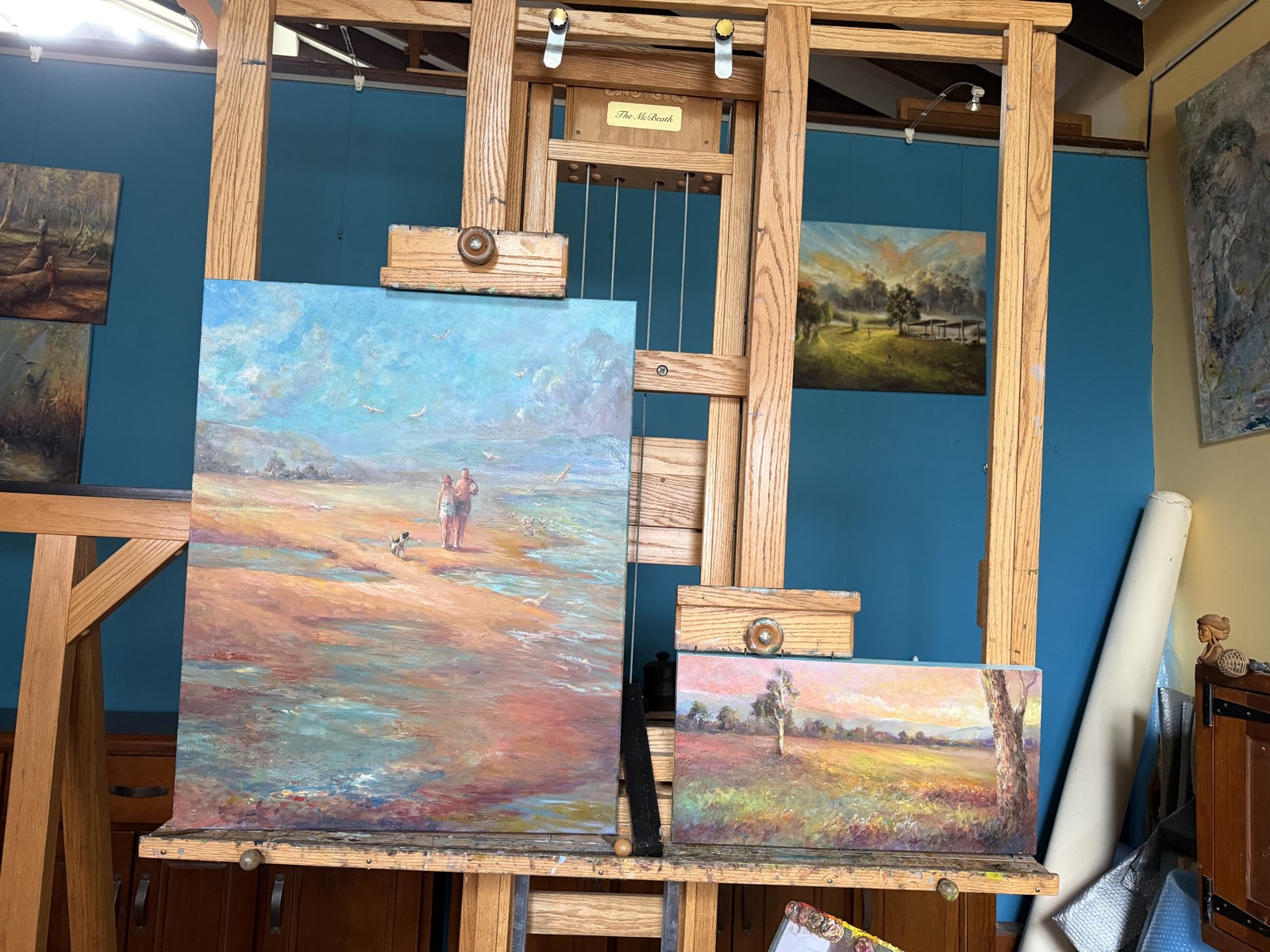 Carol D'Arcy's studio with two paintings in progress on the easel, a beach scene and a small landscape sharing a warm palette